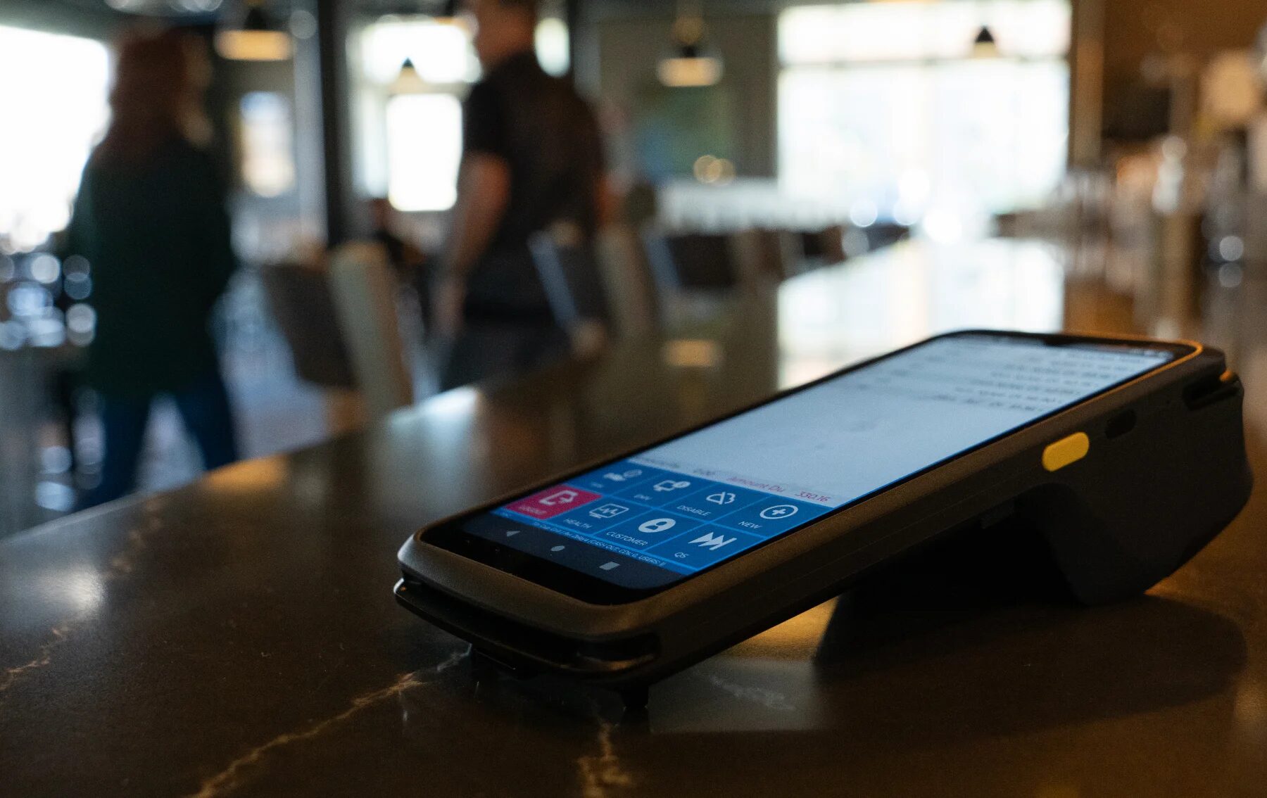 Dejavoo P8 handheld POS device on a countertop with partially visible Tonic screen showing open checks.